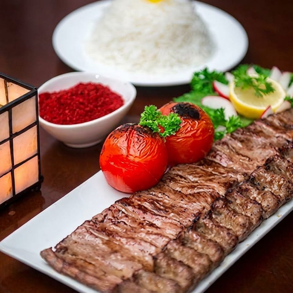 Grilled beef kebabs with roasted tomatoes, lemon, herbs, rice, red sauce, and a glowing table lantern.