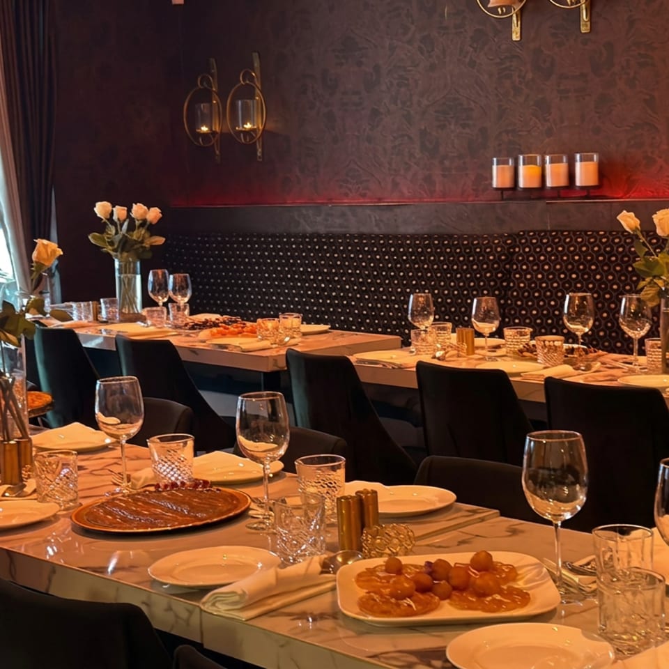 Elegant restaurant dining room with marble tables, plated dishes, wine glasses, flower arrangements, and warm candlelit decor.