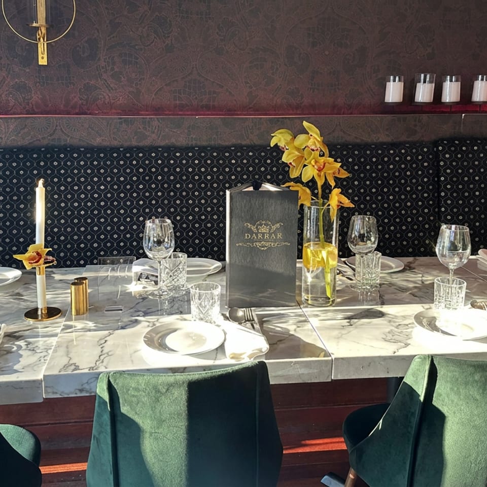 Elegant restaurant dining area with marble tables, green chairs, crystal glassware, candles, orchids, and Darbar menus.