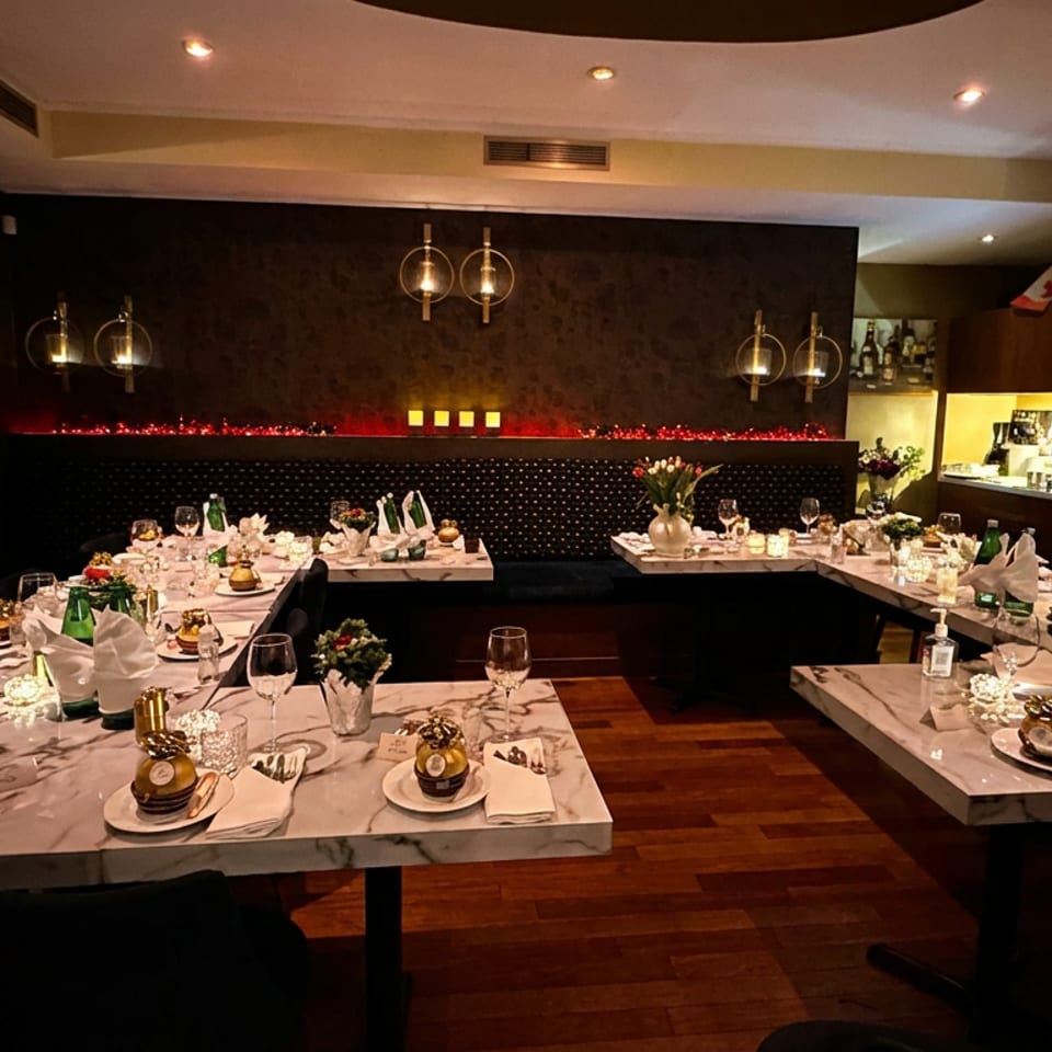 Elegant restaurant dining room with candlelit marble tables, folded napkins, glassware, plated desserts, and glowing wall sconces.