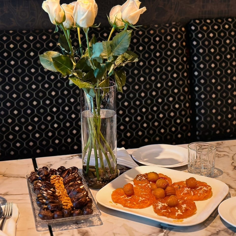 Restaurant table set with white roses, plates and glasses, featuring mussels with orange garnish and a colorful sauced dish.