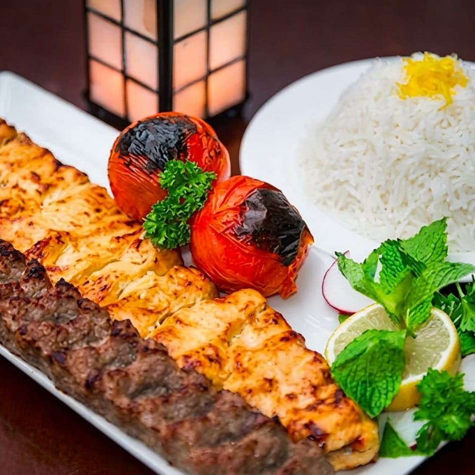 Persian mixed grill platter with minced meat and chicken kebabs, grilled tomatoes, saffron rice, herbs, lime, and radishes.